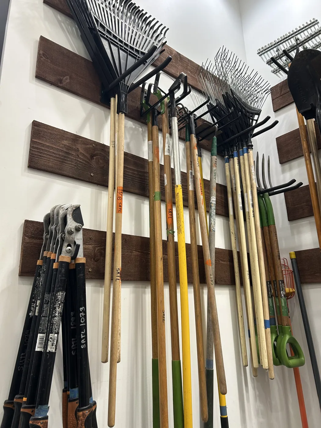 Rakes and garden tools hanging on a wooden wall rack